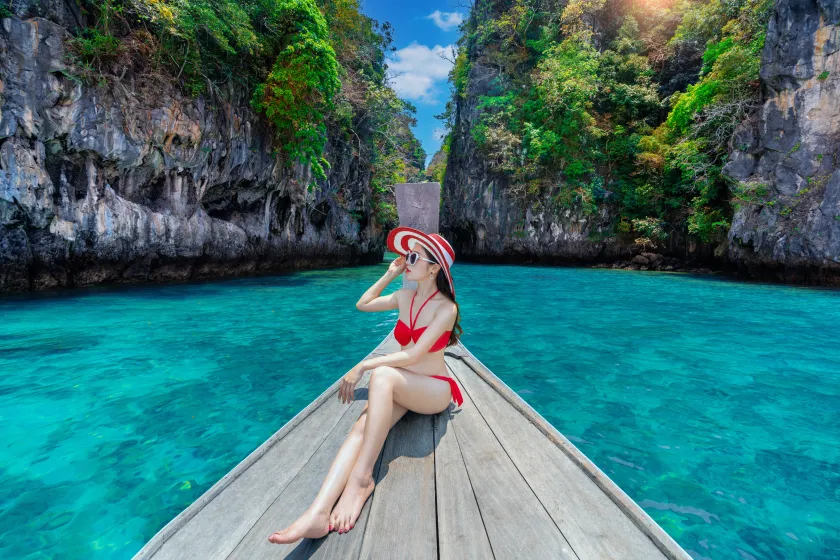 Woman in a red bikini on a traditional Thai longtail boat in a turquoise lagoon, Rawai tour&travel